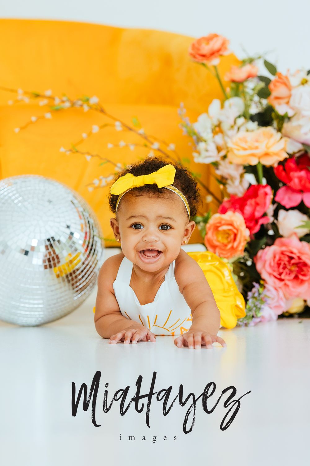 Colorful baby photo setup with disco balls and floral arrangements against orange background.