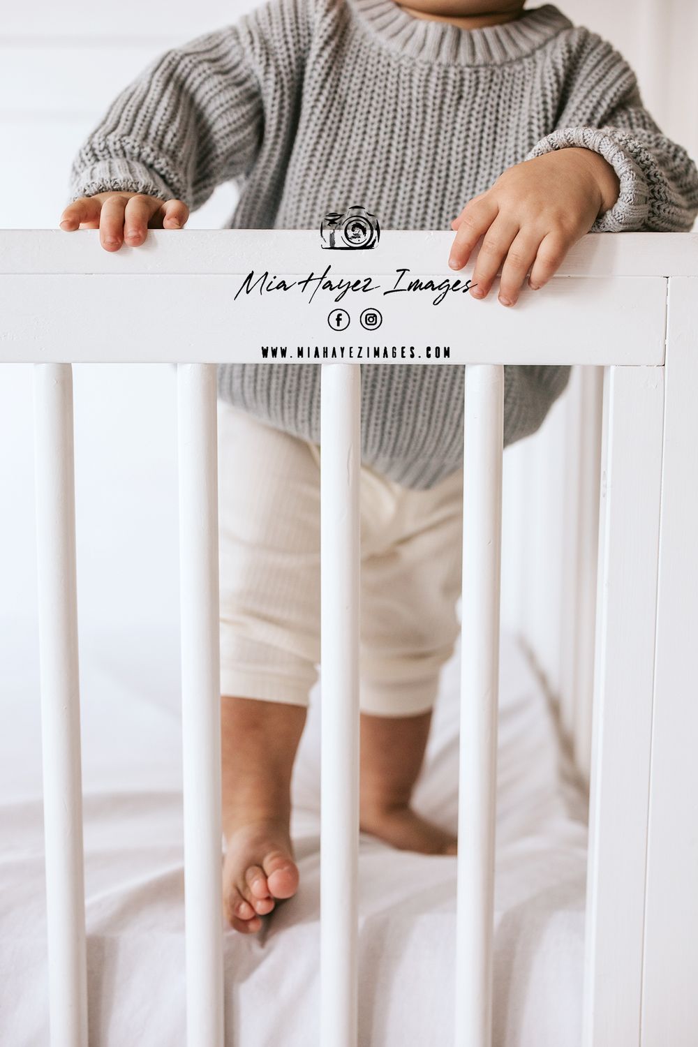 Close-up of cozy grey knit sweater against white crib railing in nursery setting.