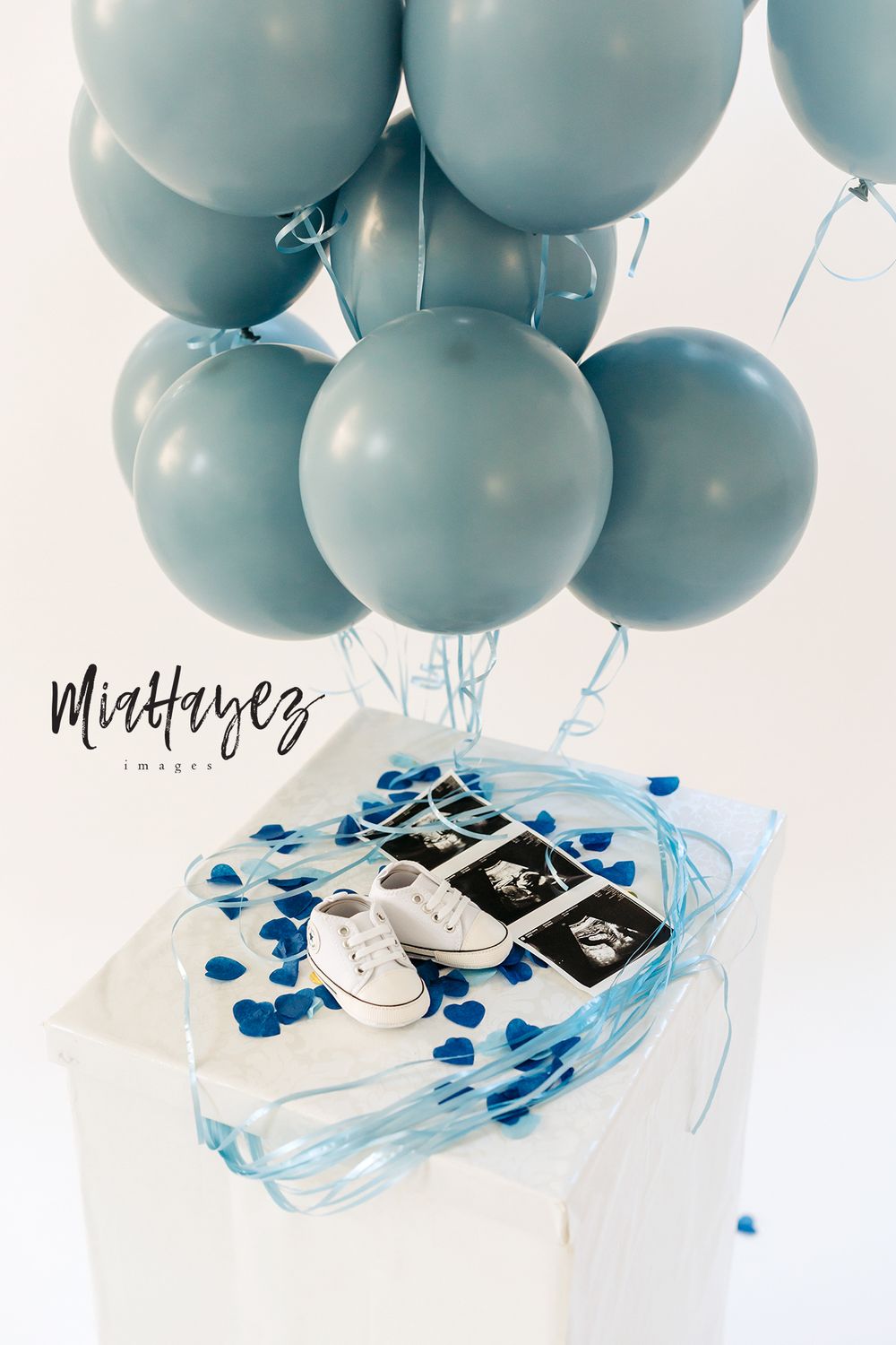 Baby announcement with blue balloons and ultrasound photos with white baby shoes.