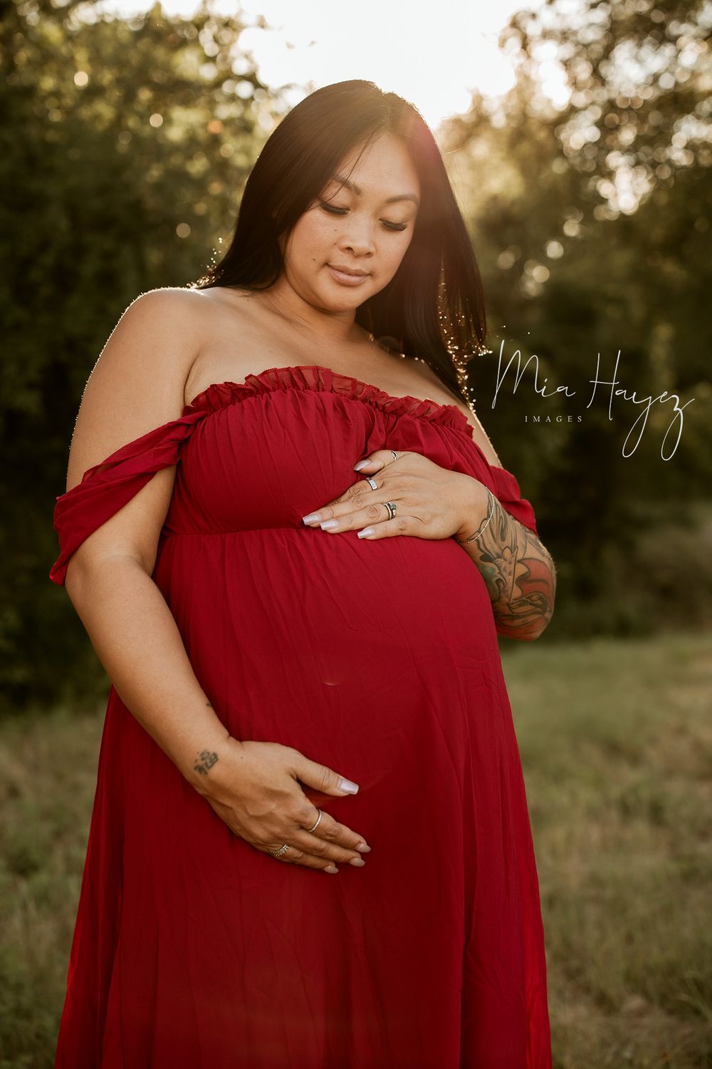 Outdoor maternity photography session at sunset featuring a flowing red dress.