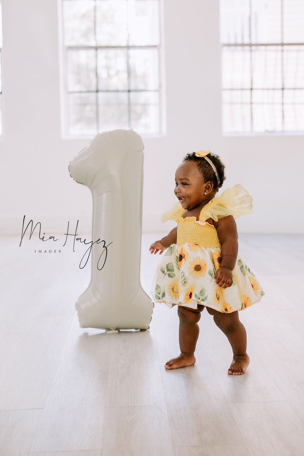 Baby in yellow outfit crawling and playing in bright white studio setting.