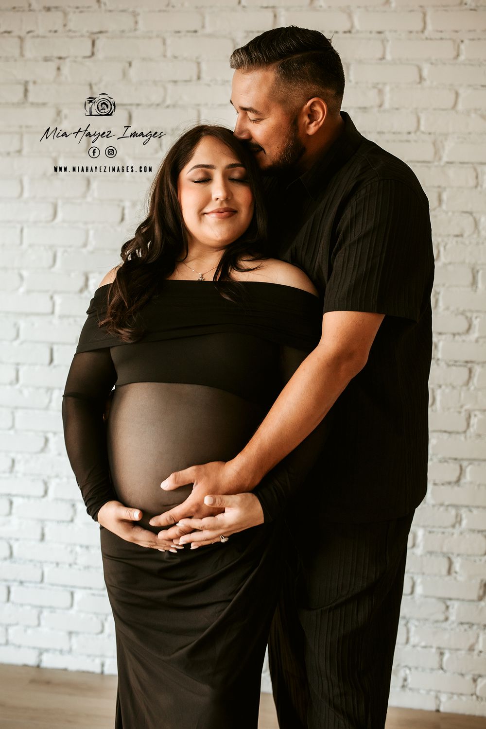 Intimate maternity session against white brick wall background.