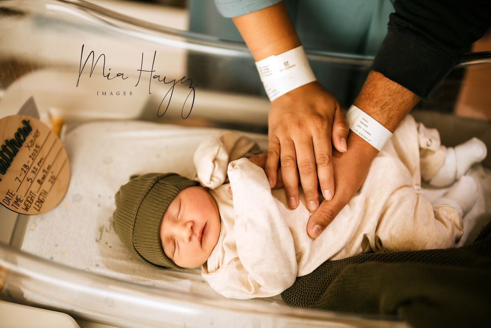 Newborn baby wearing olive green hat sleeping peacefully.