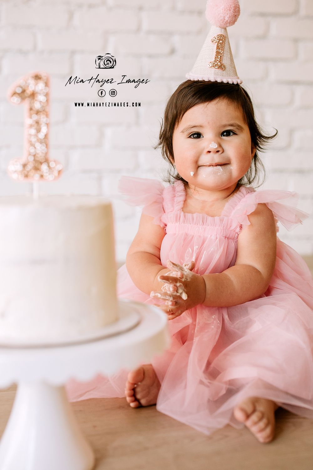 Baby wearing pink tulle dress sits on white floor during photography session.
