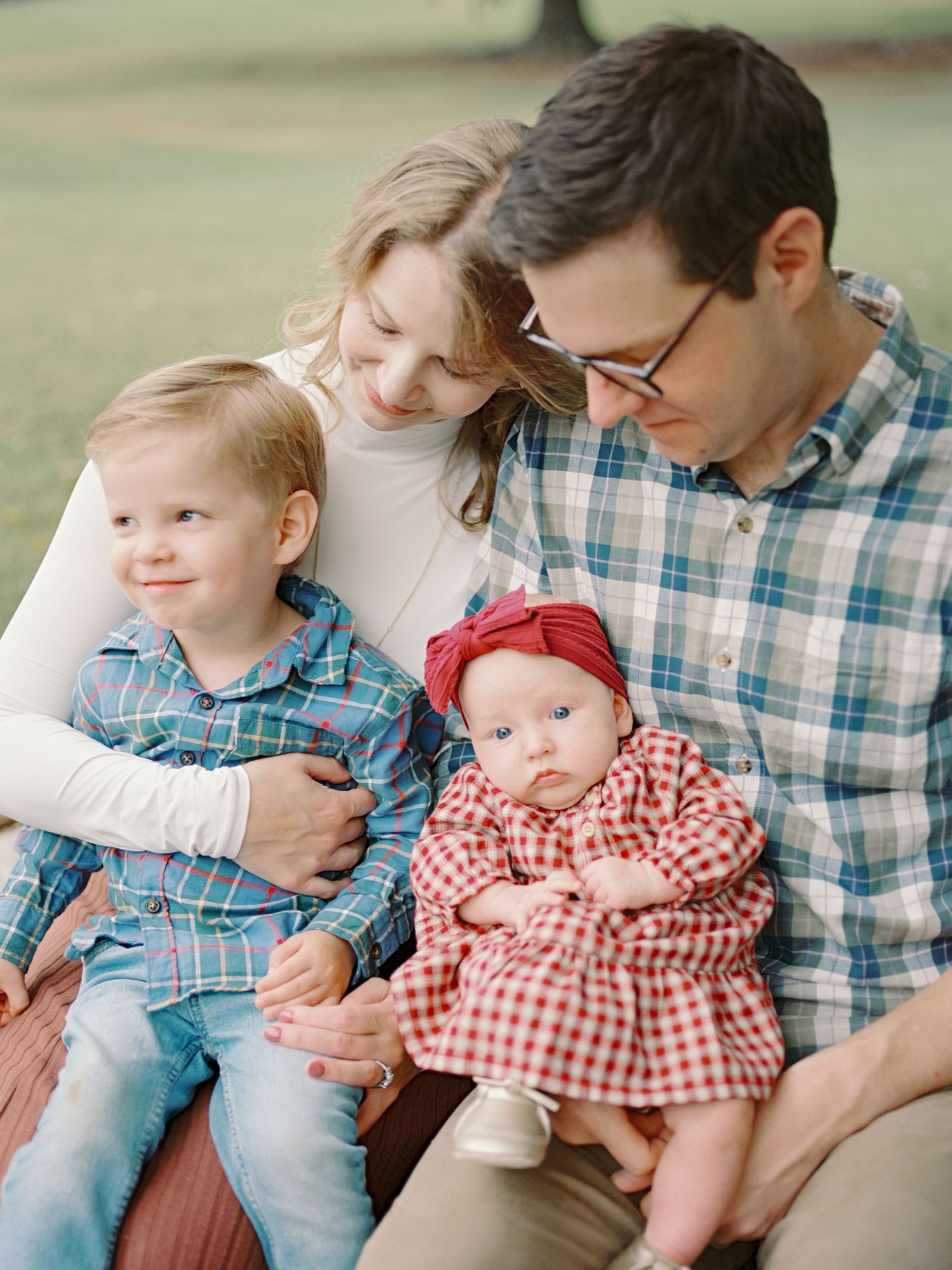 Family of four poses together in an autumn field with trees in the background, wearing coordinated outfits in earth tones.