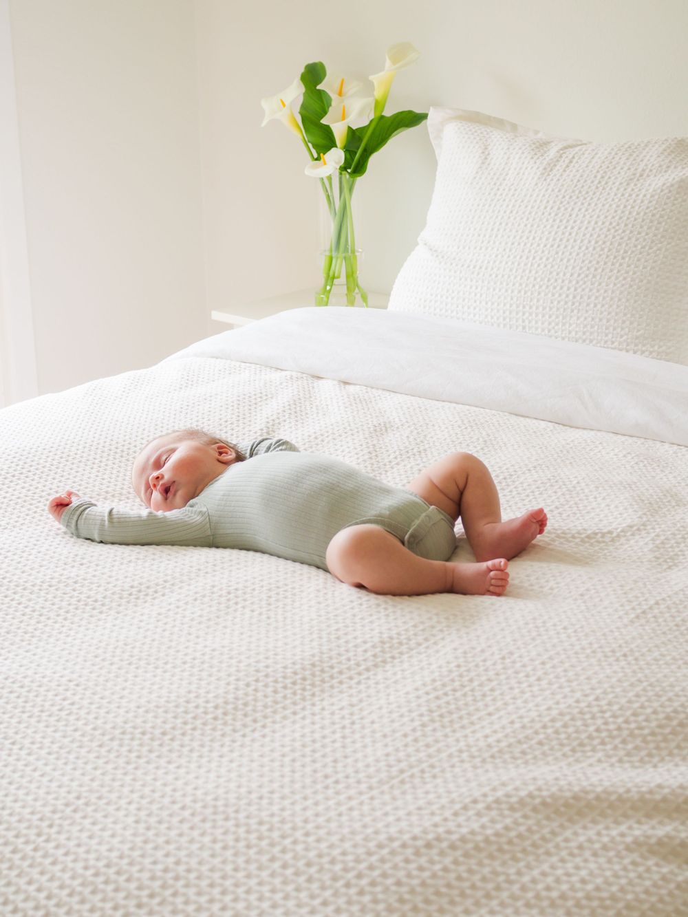 white and bright, in-home newborn session. newborn baby laying stretched out on a white bed with sun shining through window. Sonoma County
