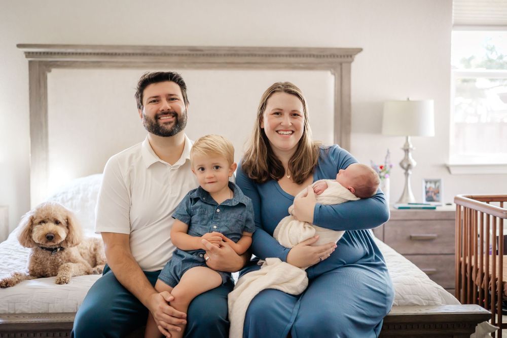 parents holding their toddler and new born baby boy at the foot of their bed. in-home newborn session in Sonoma County. family pet dog.
