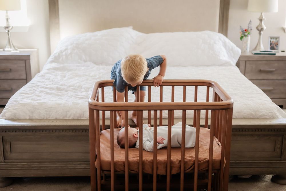 toddler boy leaning over crib to check on his newborn baby brother. in home newborn session in Sonoma county