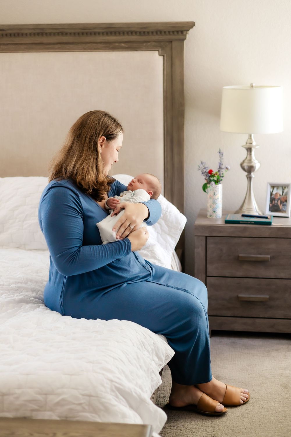 mom holding sleeping newborn while sitting on the edge of the bed with her legs crossed. Sonoma County Santa Rosa.