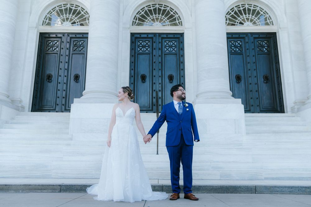 A bride and groom stand in front of ornate white stone archways and decorative blue doors at a wedding venue.