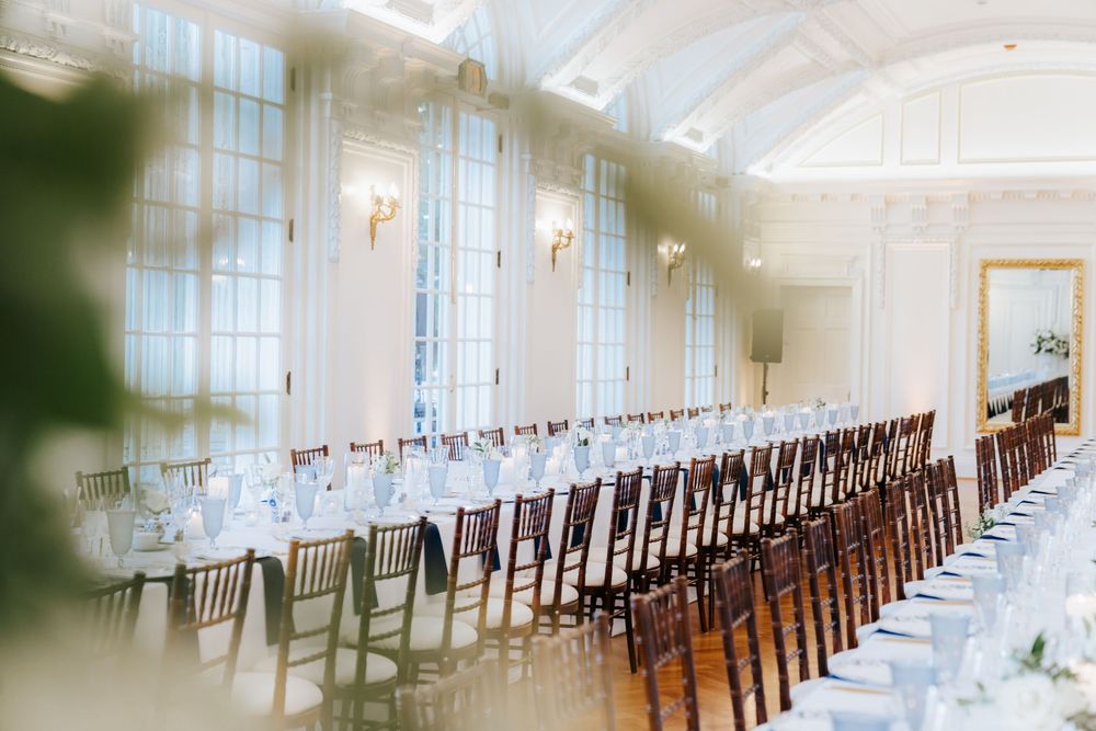 Elegant white ballroom with arched ceiling, tall windows, and rows of wooden chairs set for a formal event.