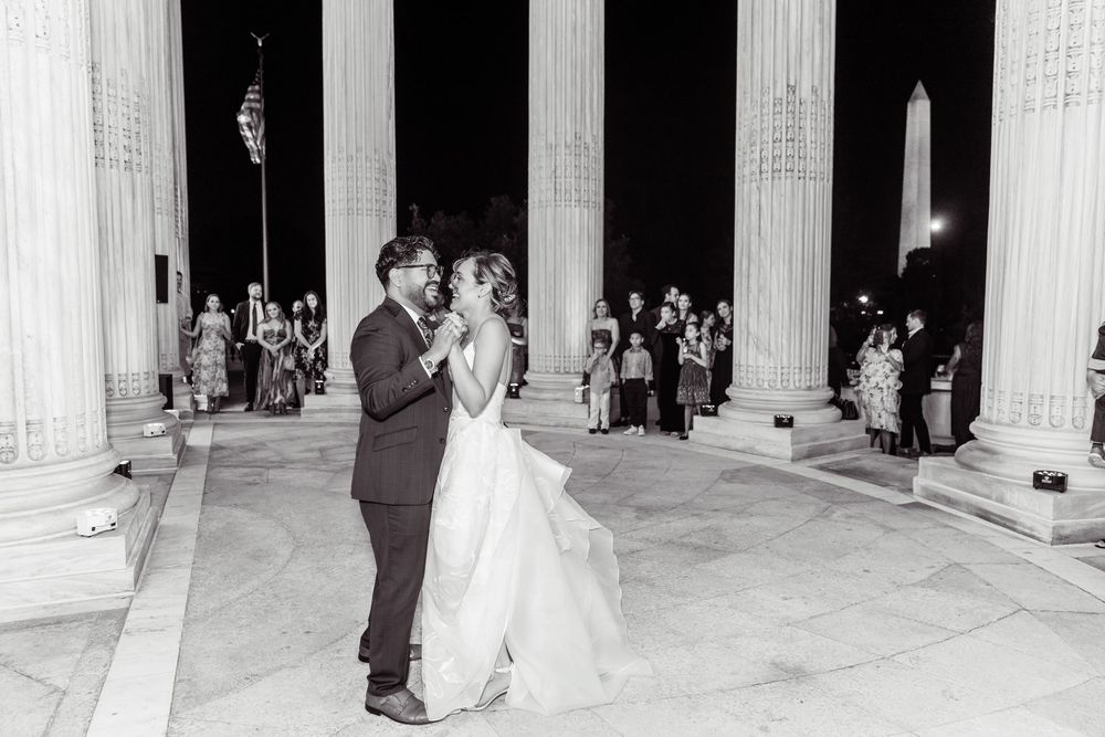 A couple shares their first dance on the steps of a grand columned building at night.
