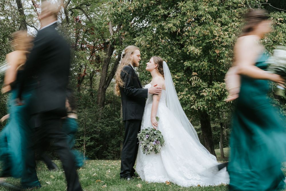 Wedding party in emerald green dresses and formal attire dances and celebrates in a lush outdoor garden setting.