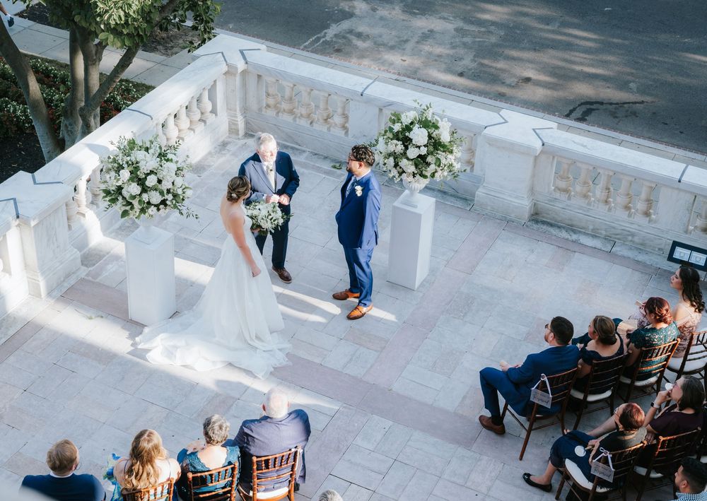 Wedding guests sit on white chairs during an outdoor ceremony overlooking a scenic coastal view.