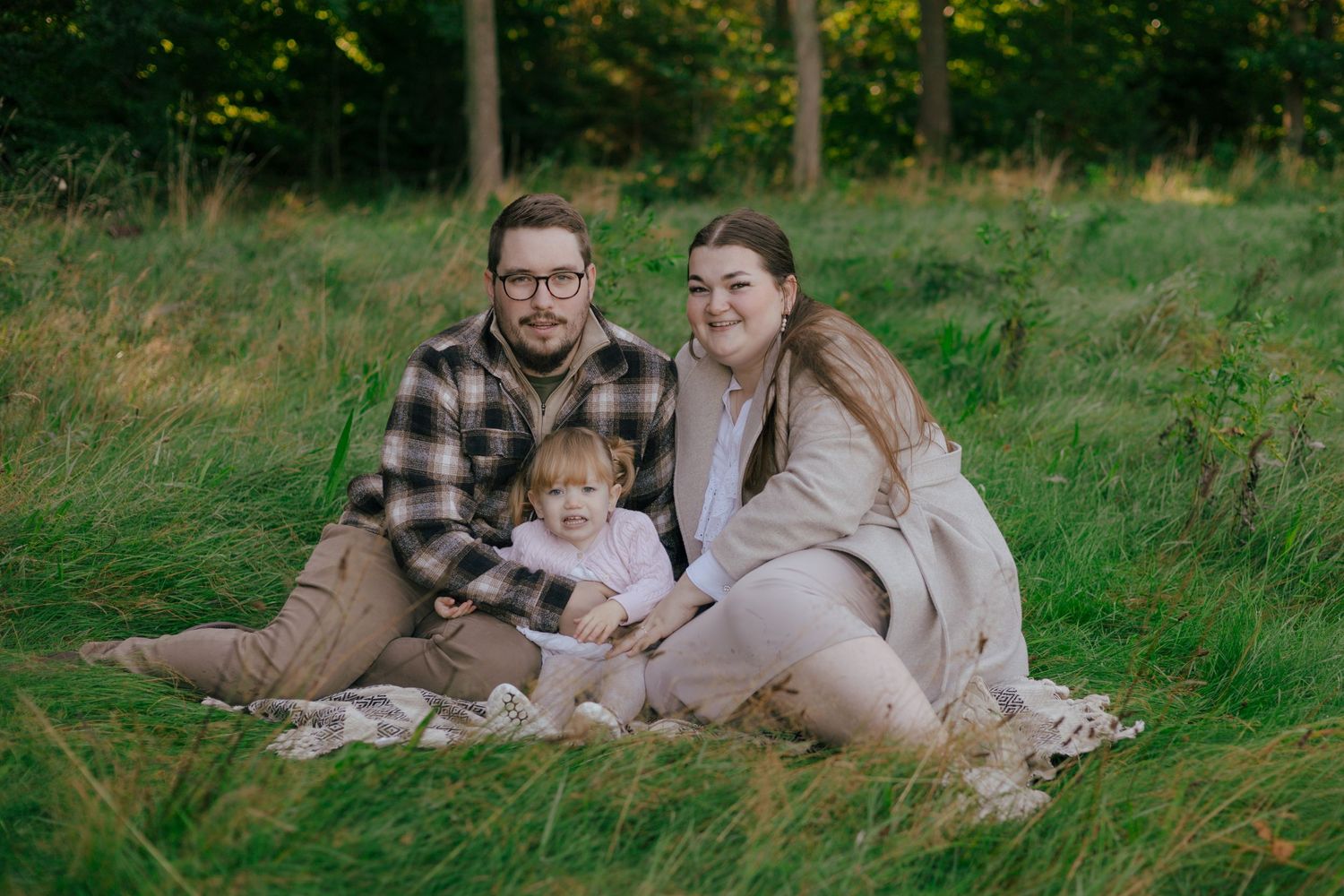 A family sitting together on a blanket in a grassy field during golden hour.