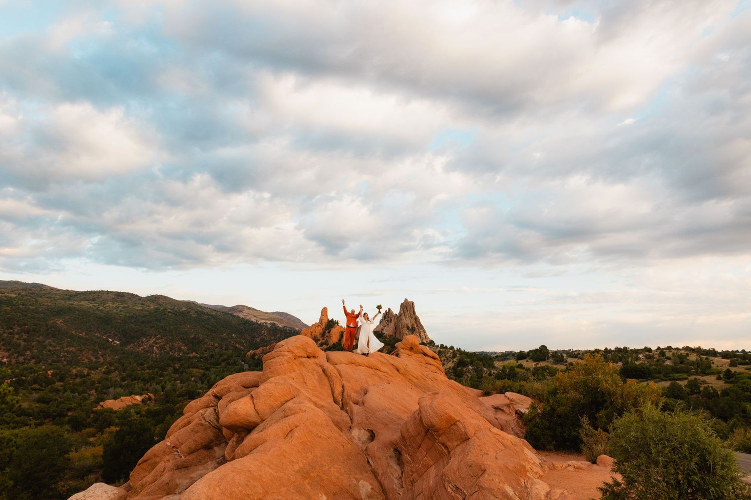 Group celebrating on red rocks formation at sunset overlooking valley.