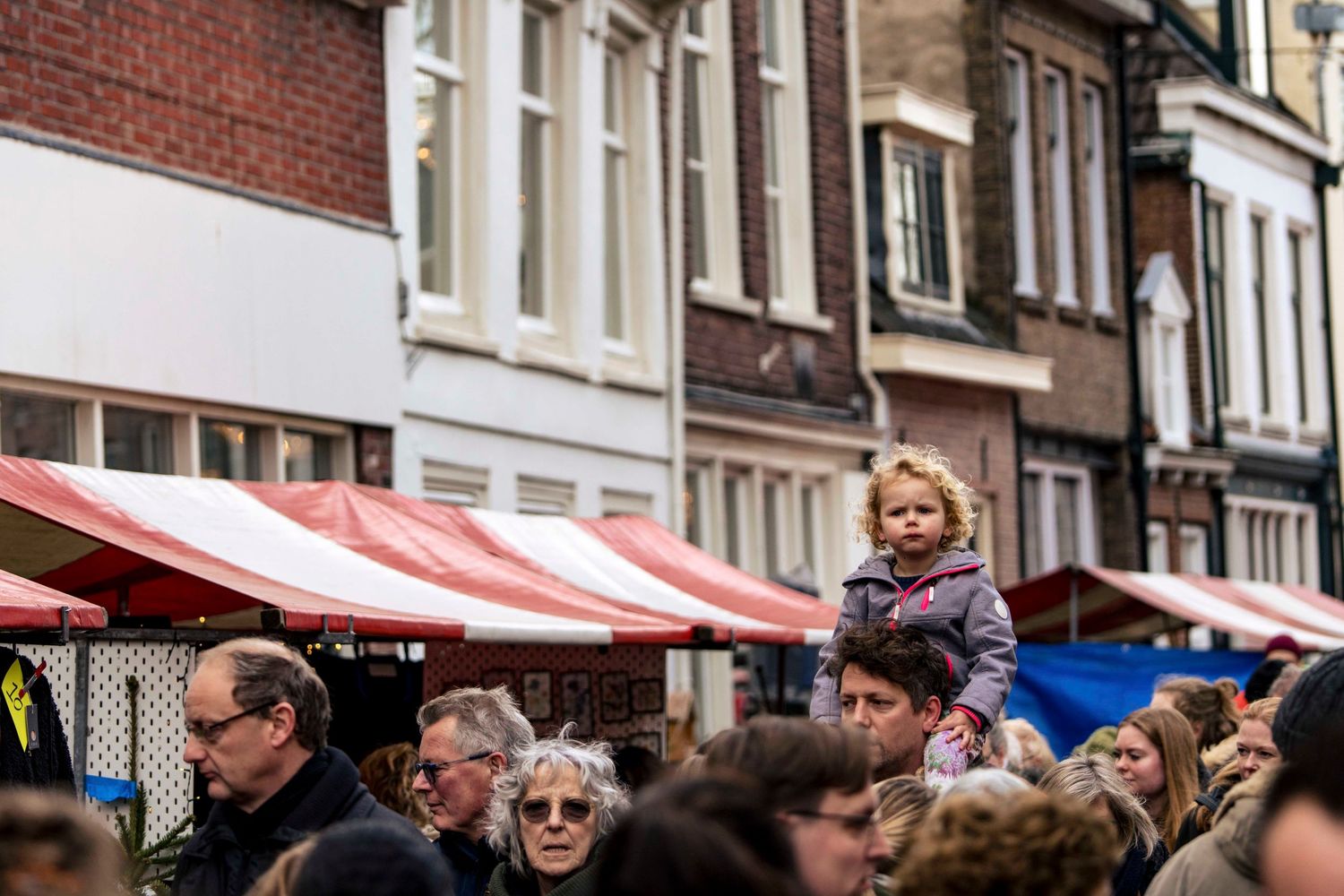 Crowded outdoor market scene with red and white striped awnings and brick buildings.