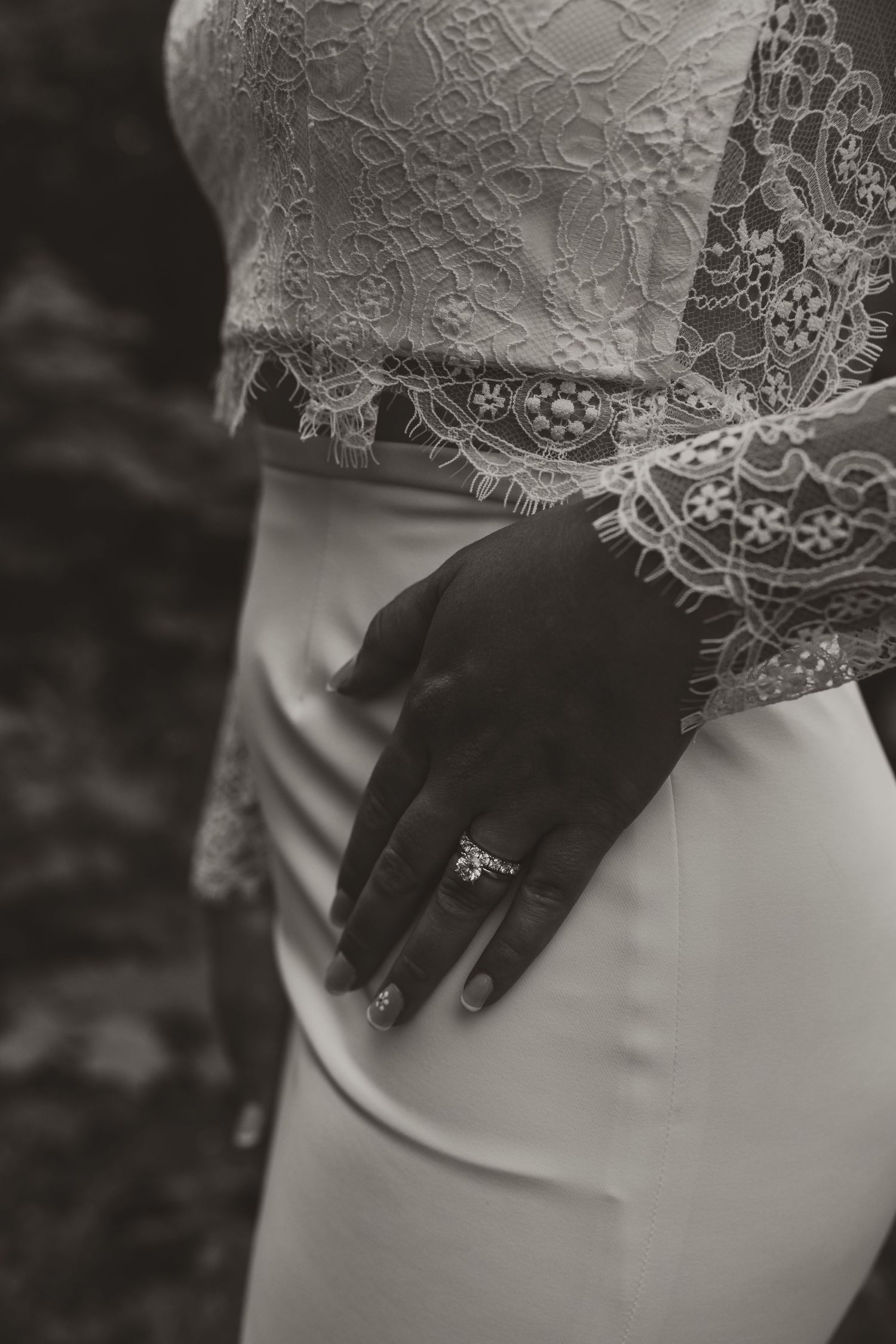 Detail shot of bride's hand with ring against lace wedding dress in black and white.