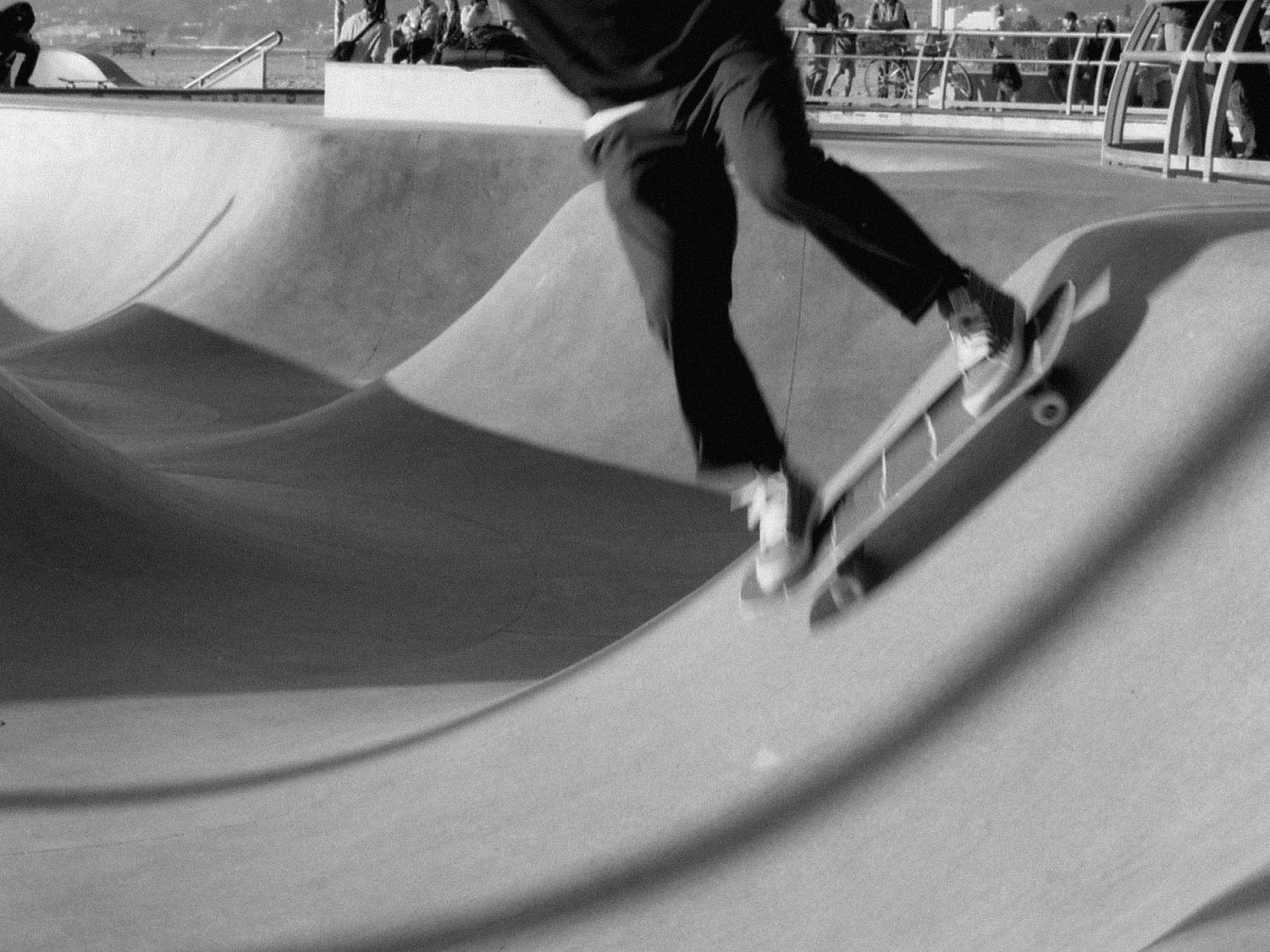 Skateboarder performs tricks in a concrete skate park ini Venice Beach shown in black and white photography.