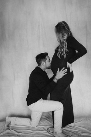 Artistic black and white maternity photo with partner kissing baby bump.