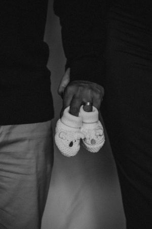Black and white photo holding tiny baby shoes against light background.
