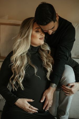 A couple embraces intimately while wearing black and dark clothing in a cozy indoor setting.