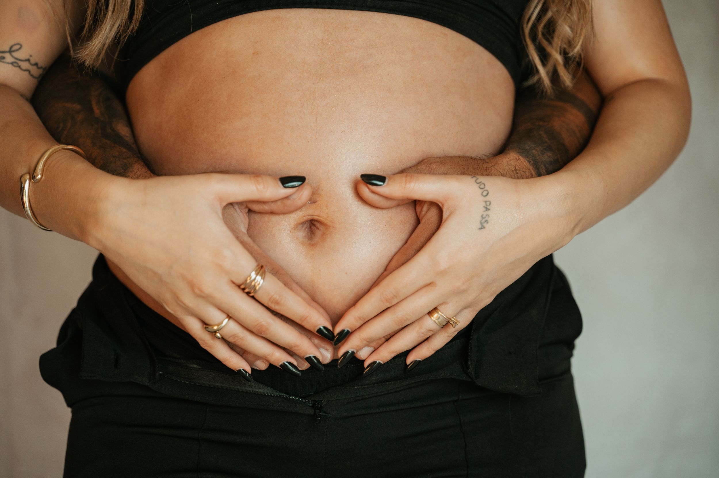 Close-up of hands forming heart shape on pregnant belly.