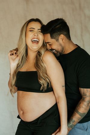 Candid maternity portrait capturing joyful laughter between couple.