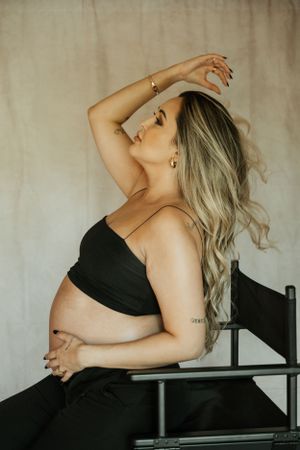 Artistic maternity portrait of woman in black outfit posing on chair.