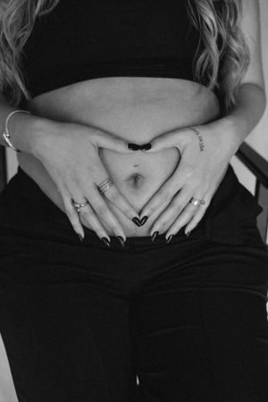 Black and white photo of hands making heart shape on pregnant belly.