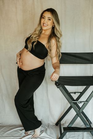 Maternity portrait showing woman in black outfit posing next to director's chair.