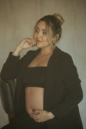 Maternity portrait featuring woman in black blazer and crop top with soft lighting.
