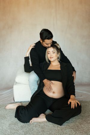 Intimate maternity portrait of couple in black clothing sitting on floor.