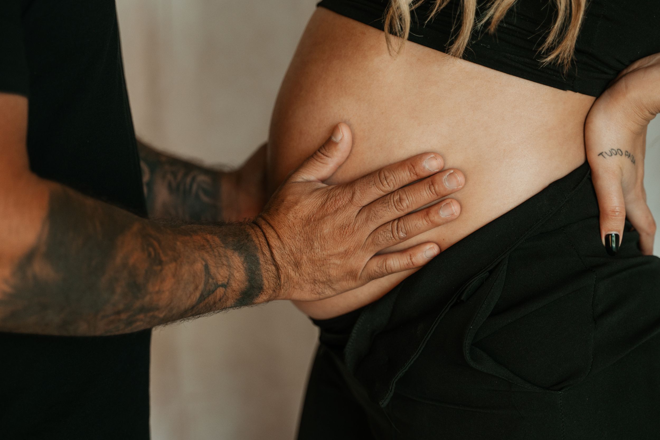 Close-up of tattooed hands touching a pregnant belly.