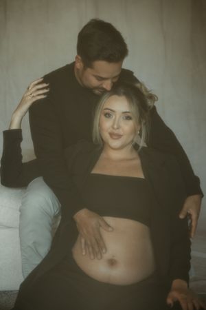 Romantic maternity photo showing couple in tender embrace against neutral background.