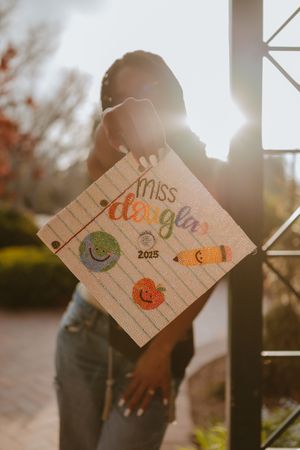A decorated graduation cap with colorful designs and text reading "Miss Deglan 2023" backlit by golden sunlight.