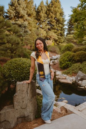 Relaxed outdoor portrait session by a pond with stone walls and evergreen trees in background.