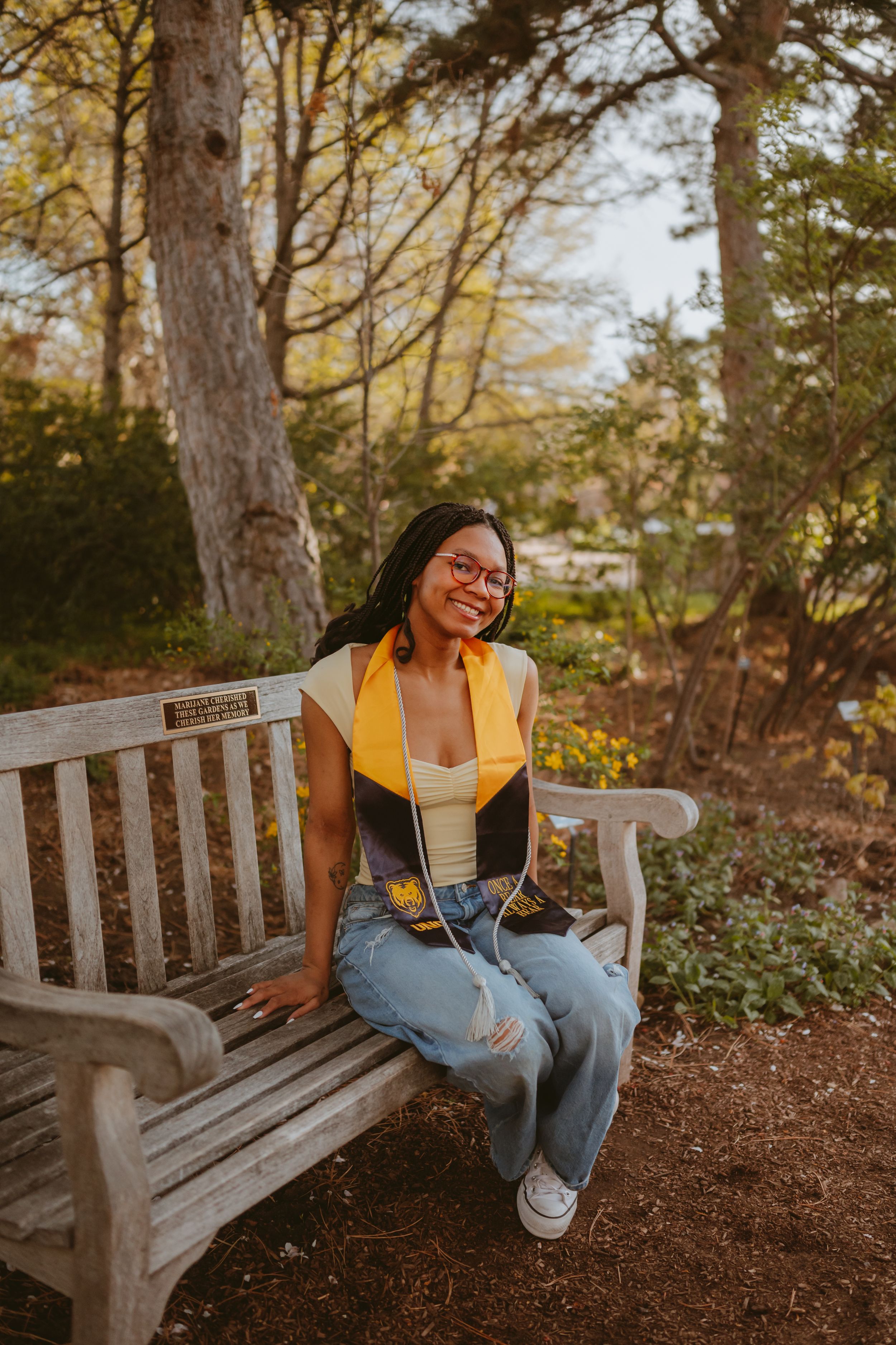 A relaxed outdoor portrait session on a wooden bench surrounded by natural foliage and dappled sunlight.