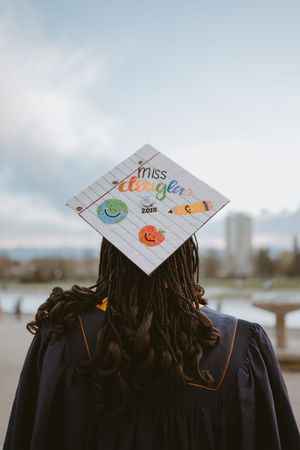 A decorated graduation cap with colorful doodles and text against a cloudy sky.