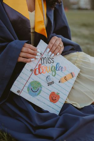 Decorated graduation cap with colorful handwritten text and cute doodles on a navy blue background.