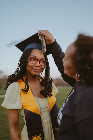 A graduation photoshoot showing academic regalia with yellow stole and navy cap.