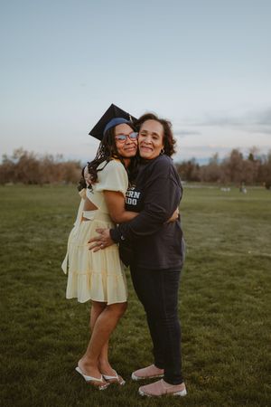 Two people sharing emotional embrace during graduation celebration in grassy field at dusk.