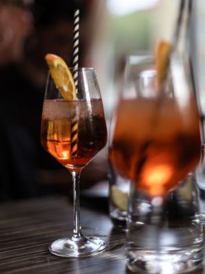Orange-tinted cocktails with garnishes in elegant wine glasses on a dark wooden table.