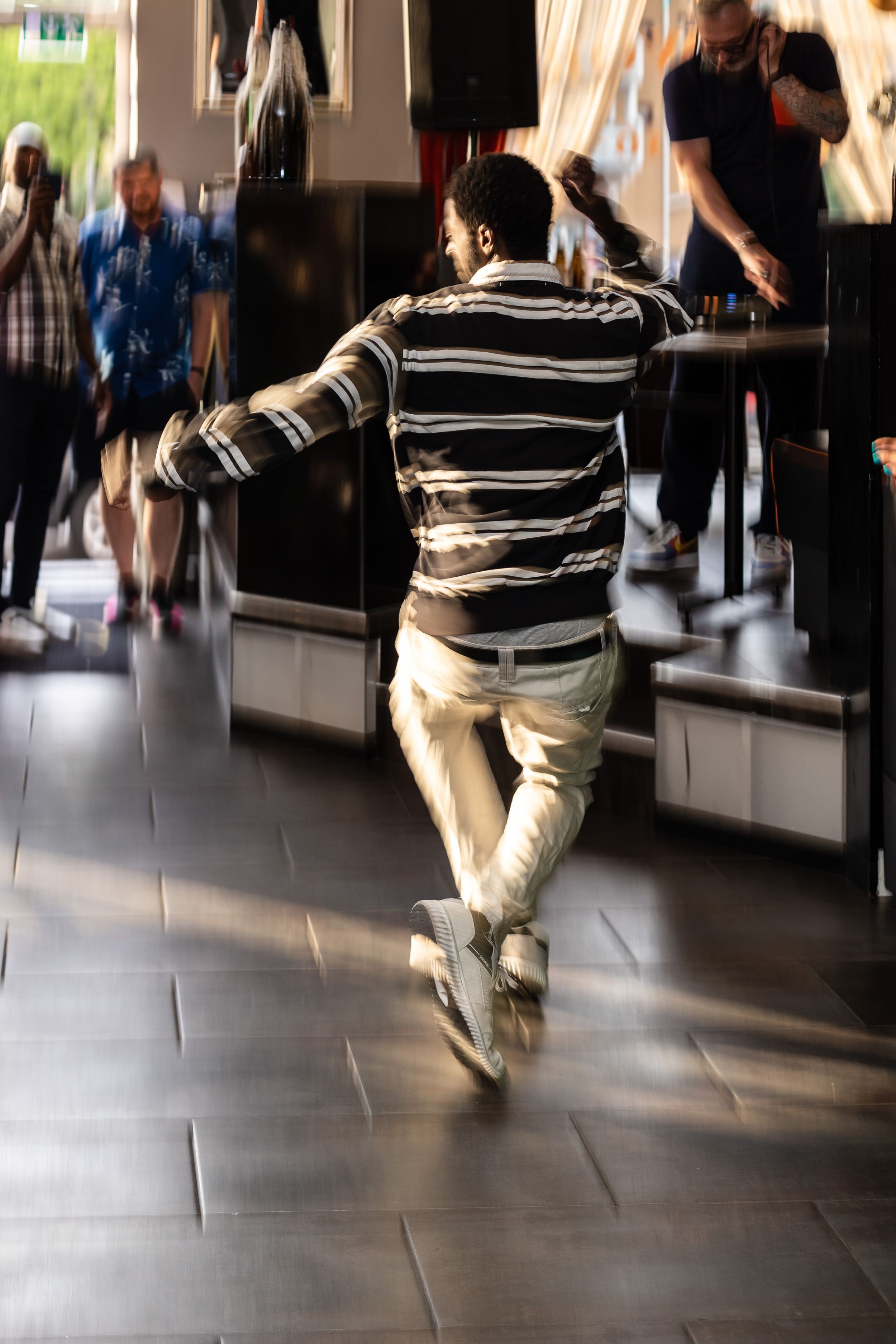 Motion-blurred dancer in striped shirt performing energetic moves on a dance floor.