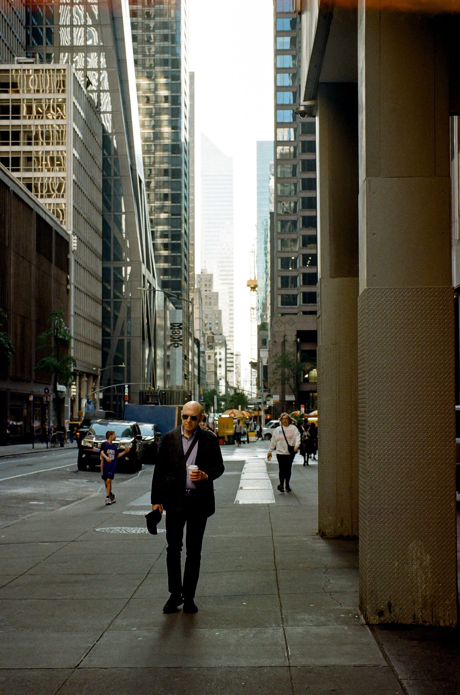 A person in business attire walks along a downtown street lined with skyscrapers and office buildings.
