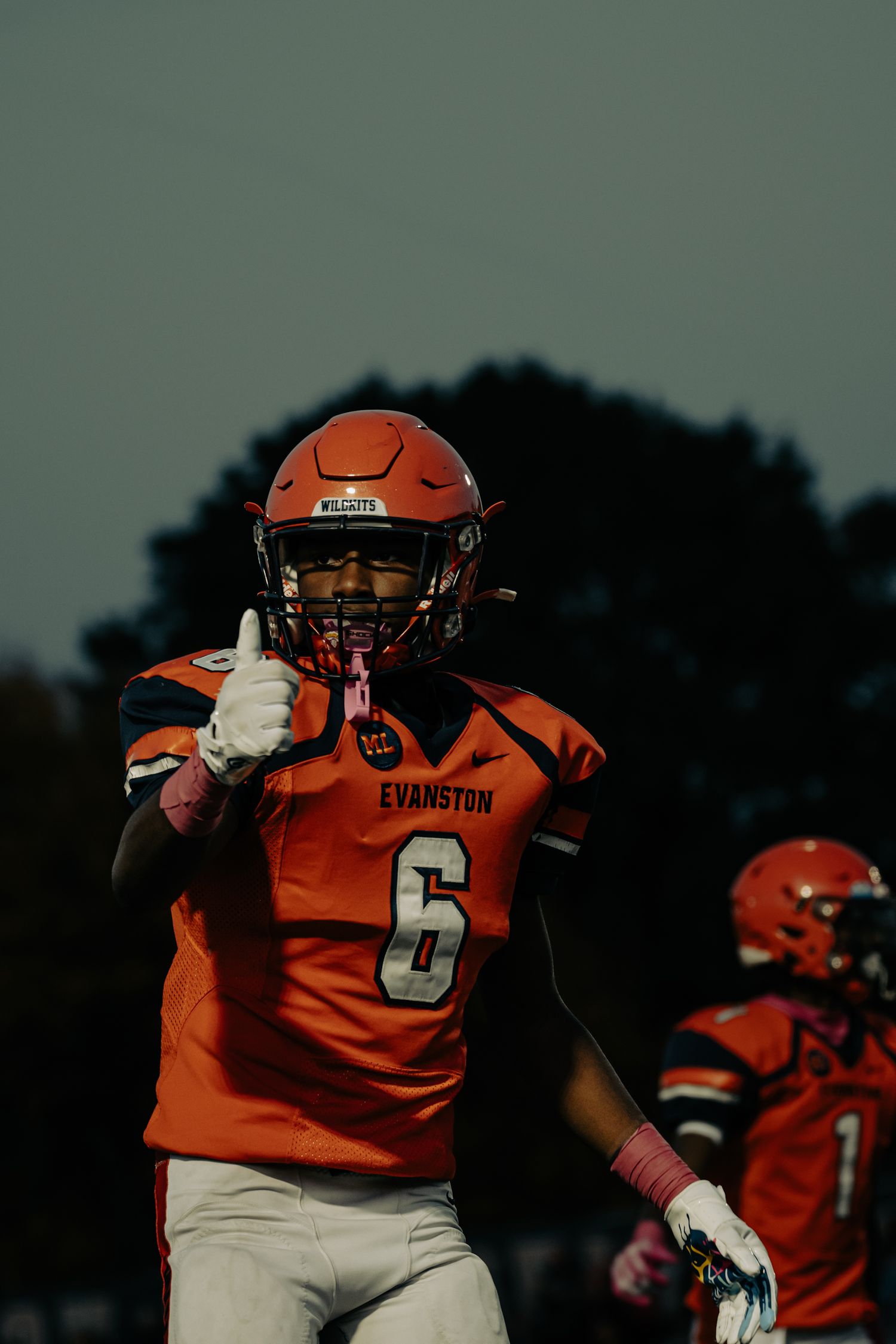 Football player in orange Evanston jersey making celebratory gesture on field during game.