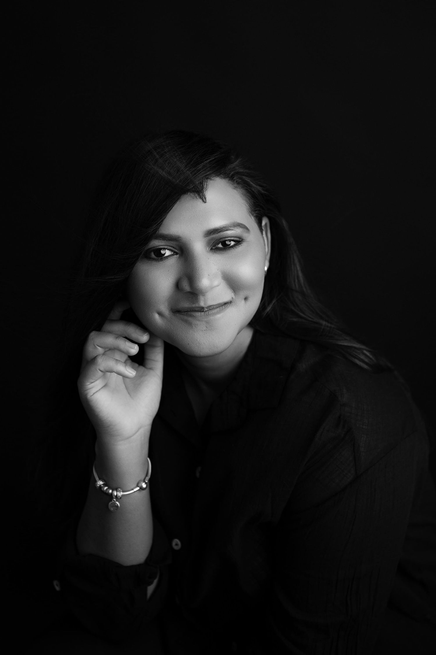 Black and white portrait showing a warm smile and gentle hand gesture against a dark background.