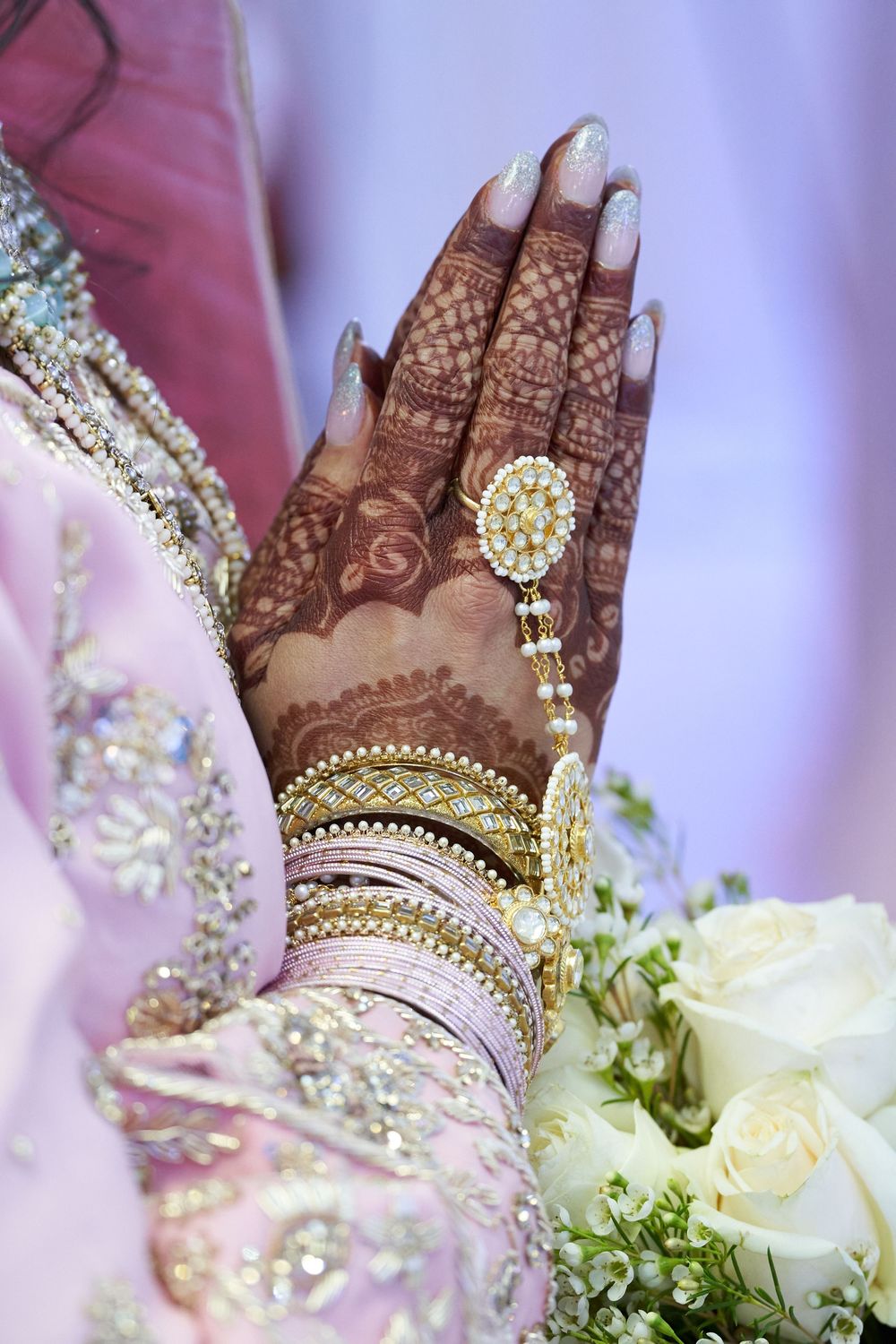 Intricate henna design adorned with gold jewelry and white floral bouquet on hands.
