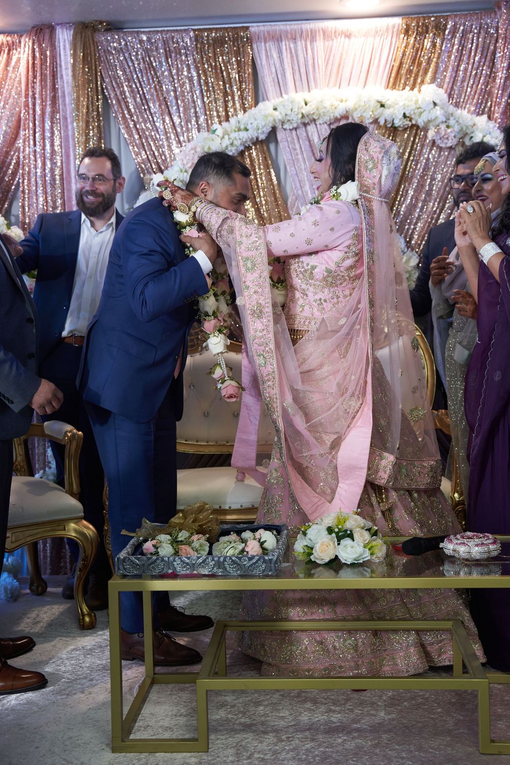 Wedding reception setup with gold sequin backdrop and guests in formal attire.