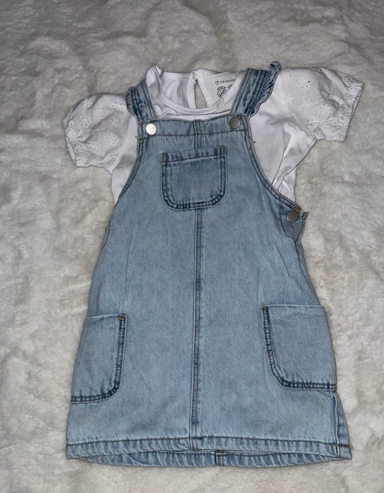 Light blue denim overall vest with white lining and pockets displayed on gray surface.